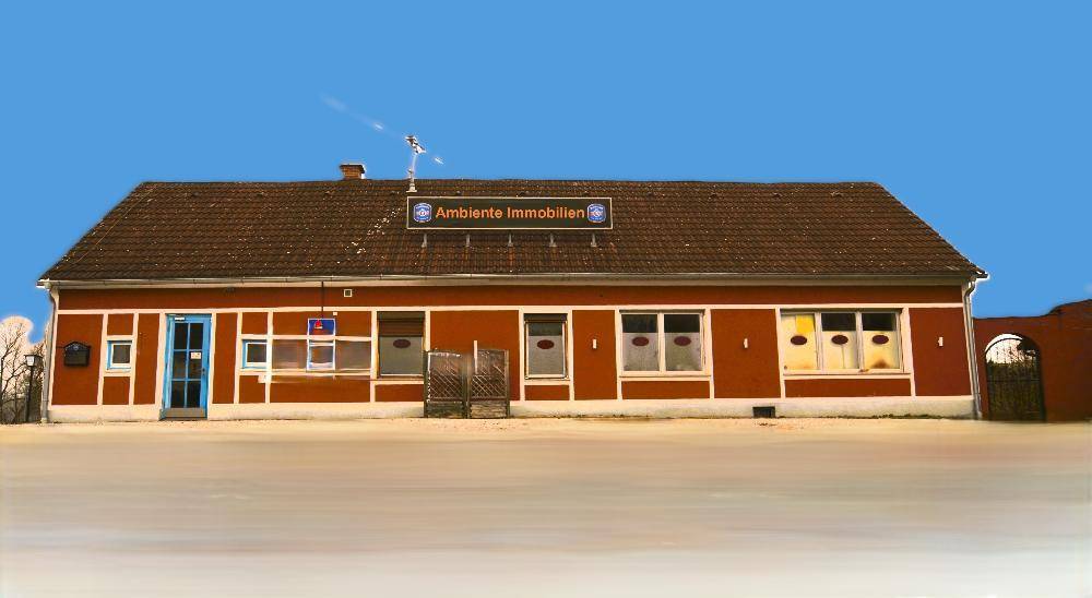 Rote Fassade eines Gebäudes mit braunem Dach und einem Firmenschild unter blauem Himmel.