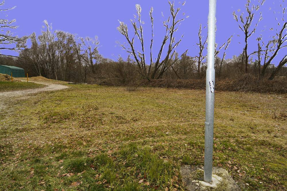 Eine weitere Ansicht einer unbefestigten, grasbewachsenen Fläche mit einem Metallpfosten und Bäumen im Hintergrund.
