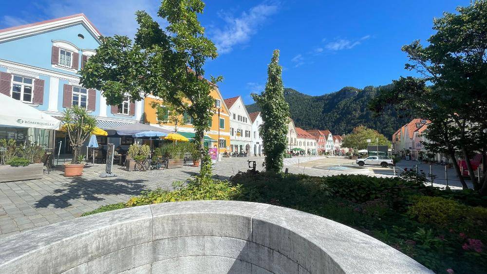 Malerische Straße mit bunten Häusern, Bäumen und Bergen unter blauem Himmel an einem sonnigen Tag.