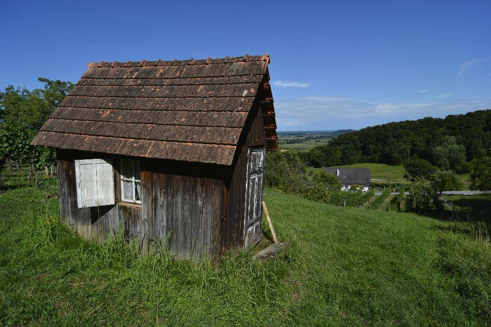 Kleiner Holzschuppen mit Ziegeldach auf einem grünen Hügel mit weitem Blick über die Landschaft.