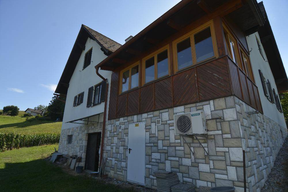 Seitenansicht des Hauses mit Steinfassade, Holzelementen und einer Klimaanlage an der Wand.