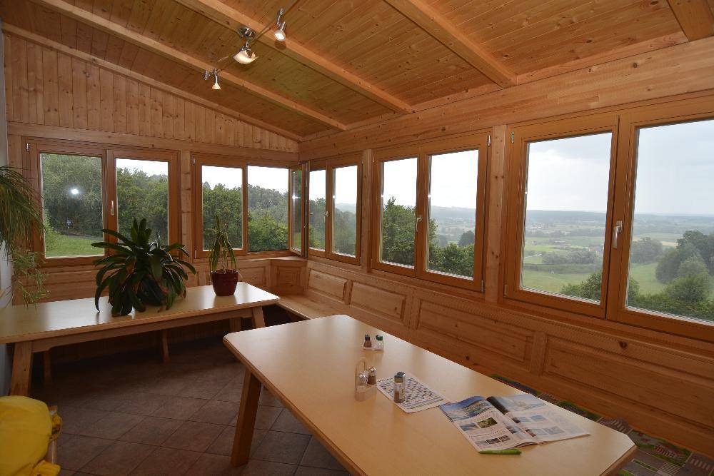 Heller Wintergarten mit Holzverkleidung und großen Fenstern, die einen weiten Ausblick auf die Landschaft bieten.