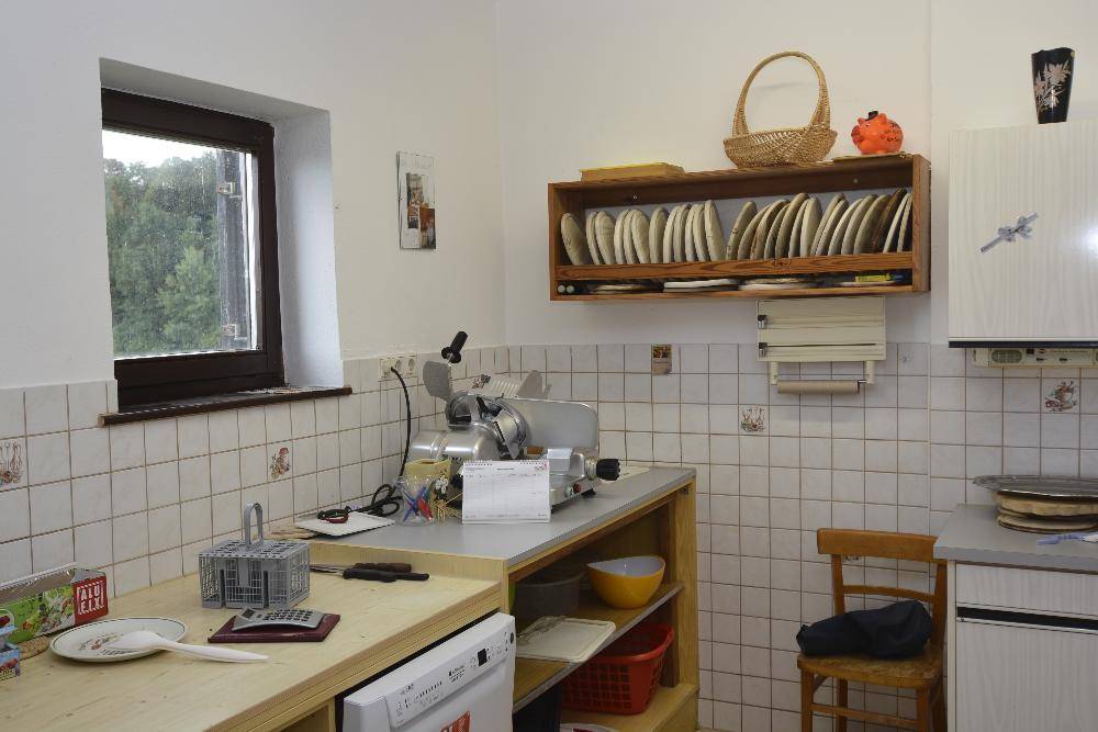 Einfache Küche mit weißen Fliesen, einem Fenster und grundlegenden Küchengeräten für den täglichen Gebrauch.