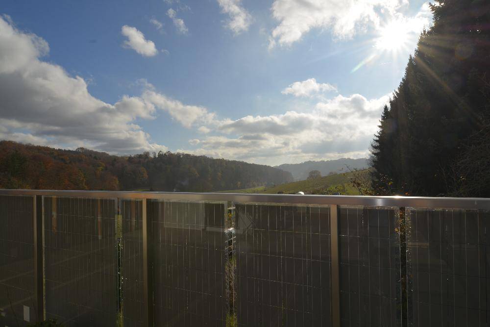 Sonniger Ausblick von der Terrasse auf die hügelige, grüne Landschaft unter blauem Himmel.