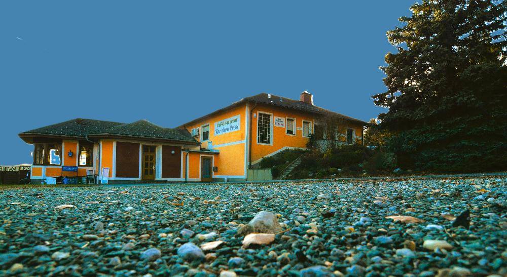 Gebäudeansicht mit gelber Fassade und Schotterfläche im Vordergrund unter blauem Himmel.