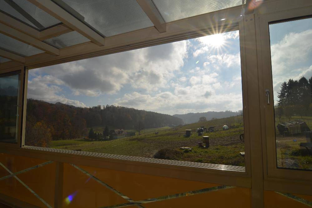 Weitläufiger Ausblick aus dem Wintergarten über die grüne, hügelige Landschaft.