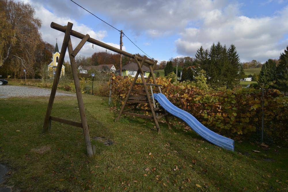 Kinderspielplatz mit Schaukel und Rutsche in einer grünen Umgebung.