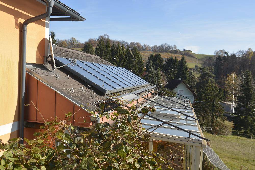 Dachansicht des Hauses mit Solarpaneelen und verglastem Wintergarten darunter.