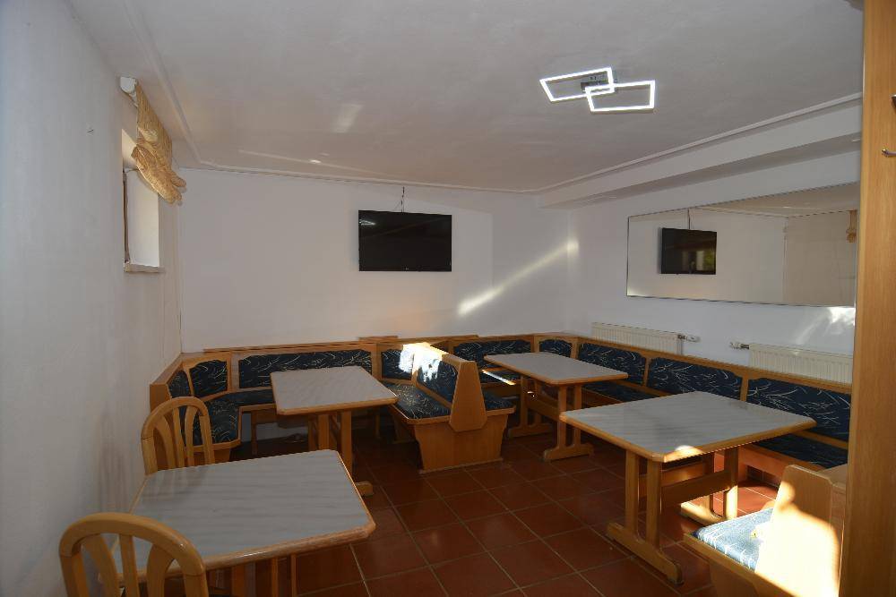Gemütlicher Raum mit Eckbänken, Tischen und Wandfernseher, ideal für gesellige Runden.