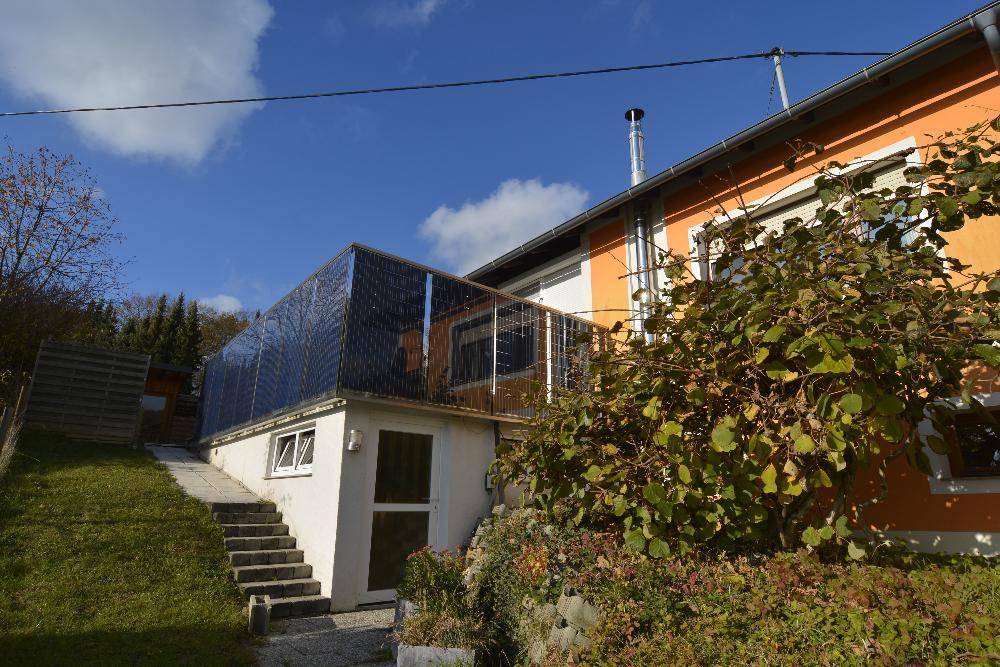 Seitenansicht des Hauses mit Außentreppe, Wintergarten und umgebender Natur.