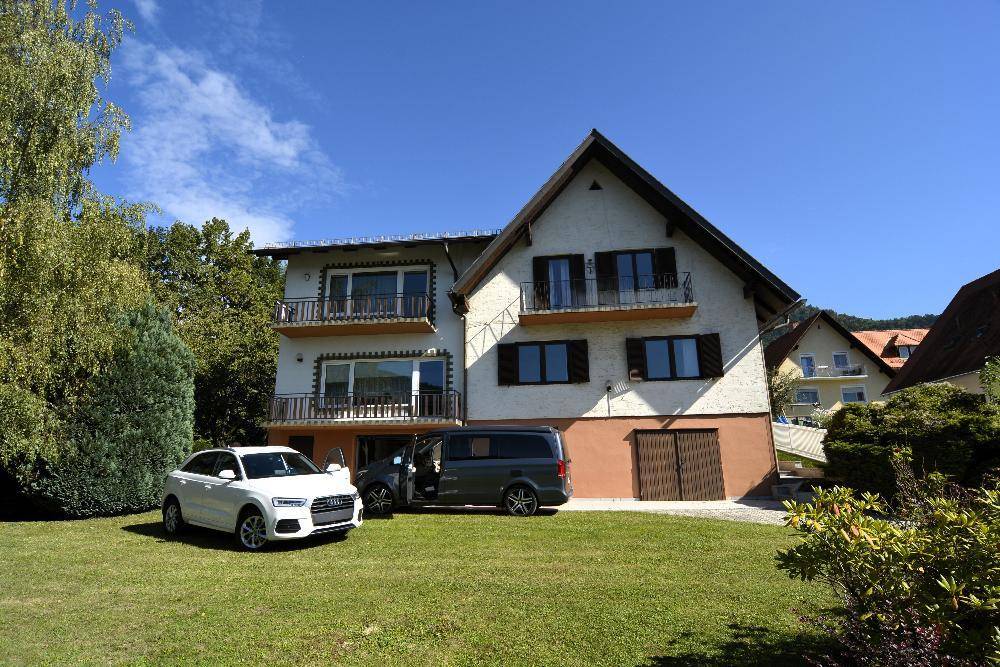 Freistehendes Haus mit großem Rasenbereich und zwei geparkten Autos vor der Garage.