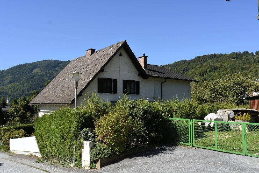 Einfamilienhaus mit Satteldach, umgeben von üppigem Grün und einem grünen Maschendrahtzaun.