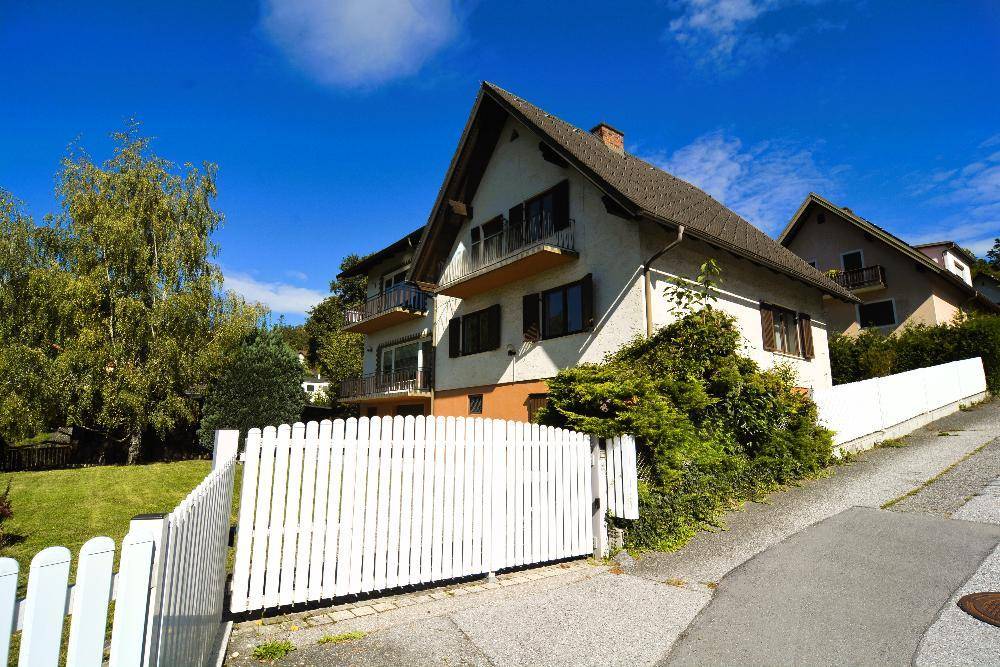 Traditionelles Wohnhaus mit Balkonen und weißem Lattenzaun unter strahlend blauem Himmel.