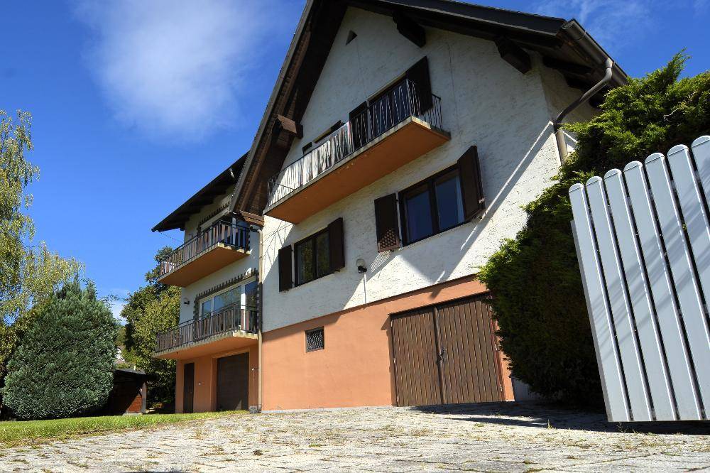 Ansicht des Hauses mit Balkonen und Garagentoren, umgeben von grünen Büschen und einem Zaun.