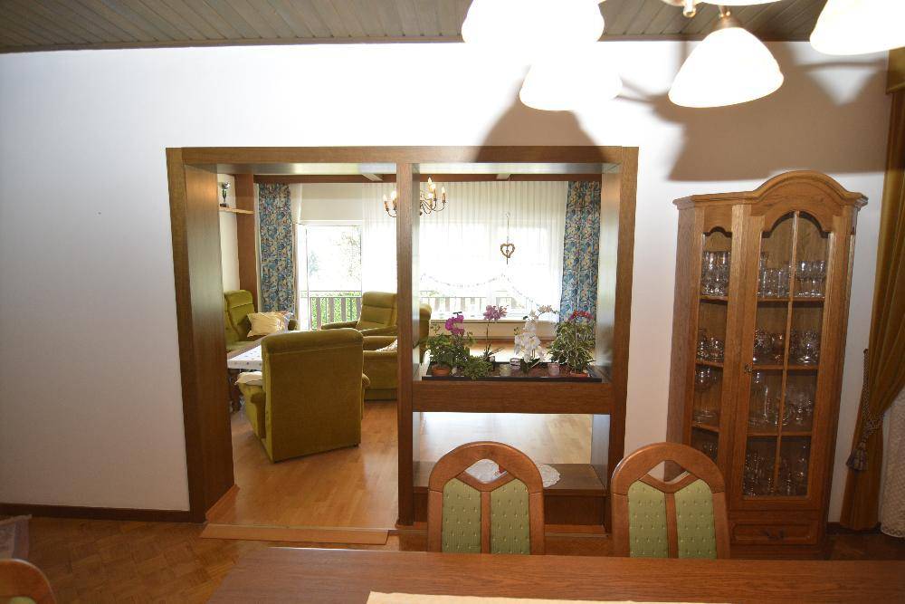 Essbereich mit Holzelementen, der in ein gemütliches Wohnzimmer mit grünen Sesseln übergeht.
