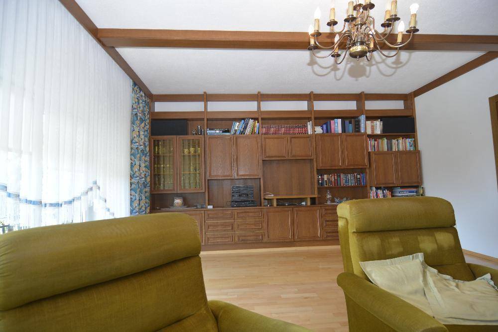 Wohnzimmer mit großer Holzschrankwand, Parkettboden und bequemen Sesseln in Grüntönen.