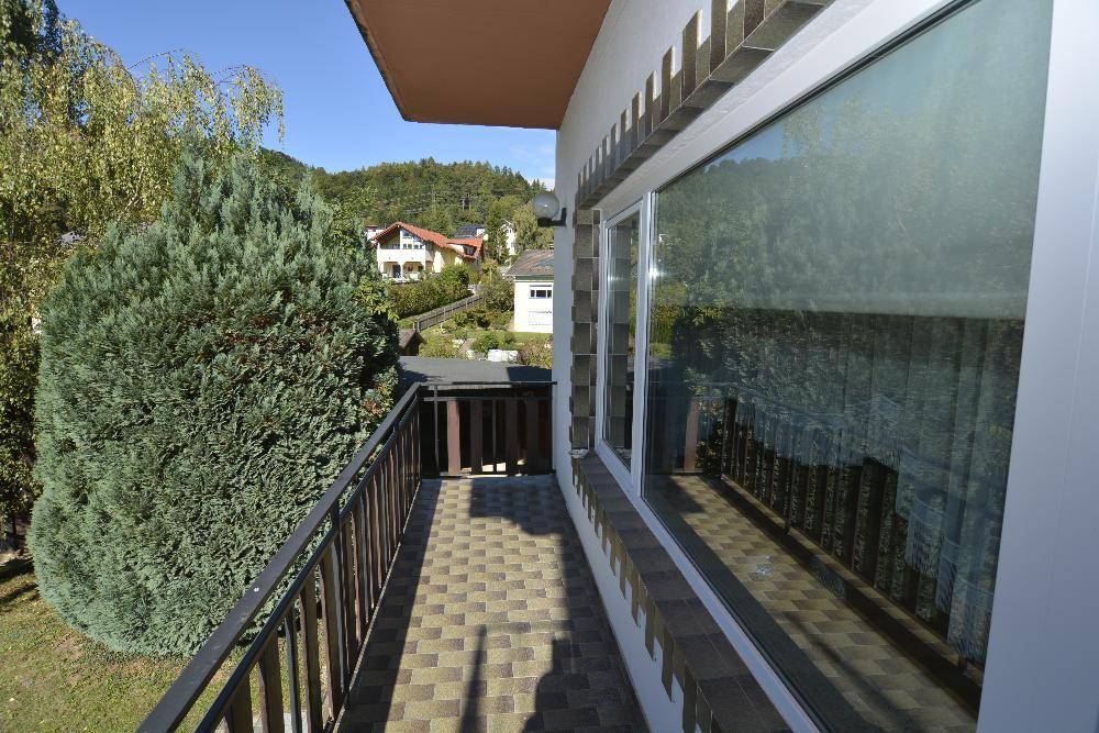 Balkon mit Fliesenboden und Blick auf die grüne Umgebung und benachbarte Häuser.