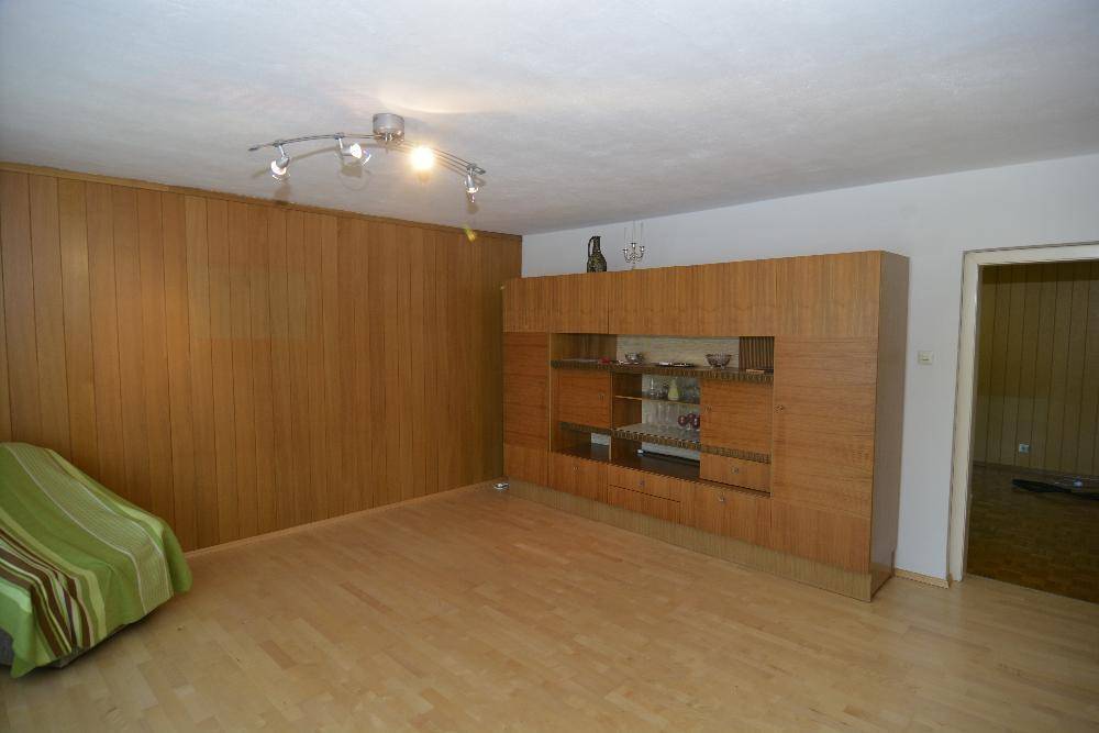 Raum mit Holztäfelung an einer Wand, Parkettboden und einem modernen Deckenstrahler.