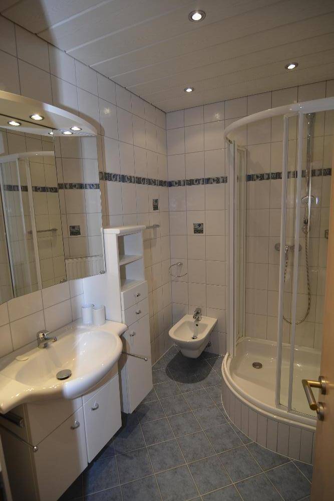 Modernisiertes Badezimmer mit Duschkabine, Bidet und hellblauen Fliesen.