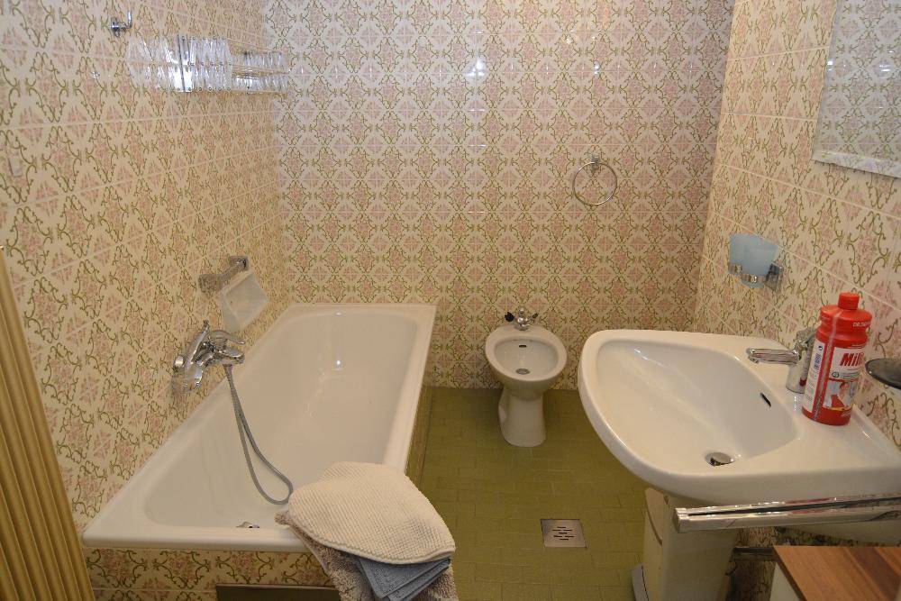 Badezimmer im 80er-Jahre-Stil mit Badewanne, Bidet und gemusterten Fliesen in Pastelltönen.