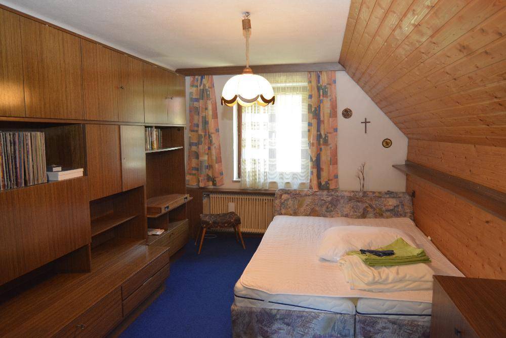 Gemütliches Schlafzimmer mit Dachschräge, Teppichboden und Holzverkleidung an der Decke.