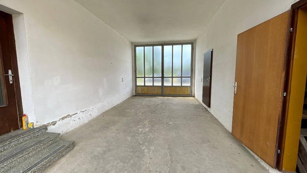 Leerer Raum mit Betonboden und großen Glastüren, möglicherweise eine Garage oder Werkstatt.