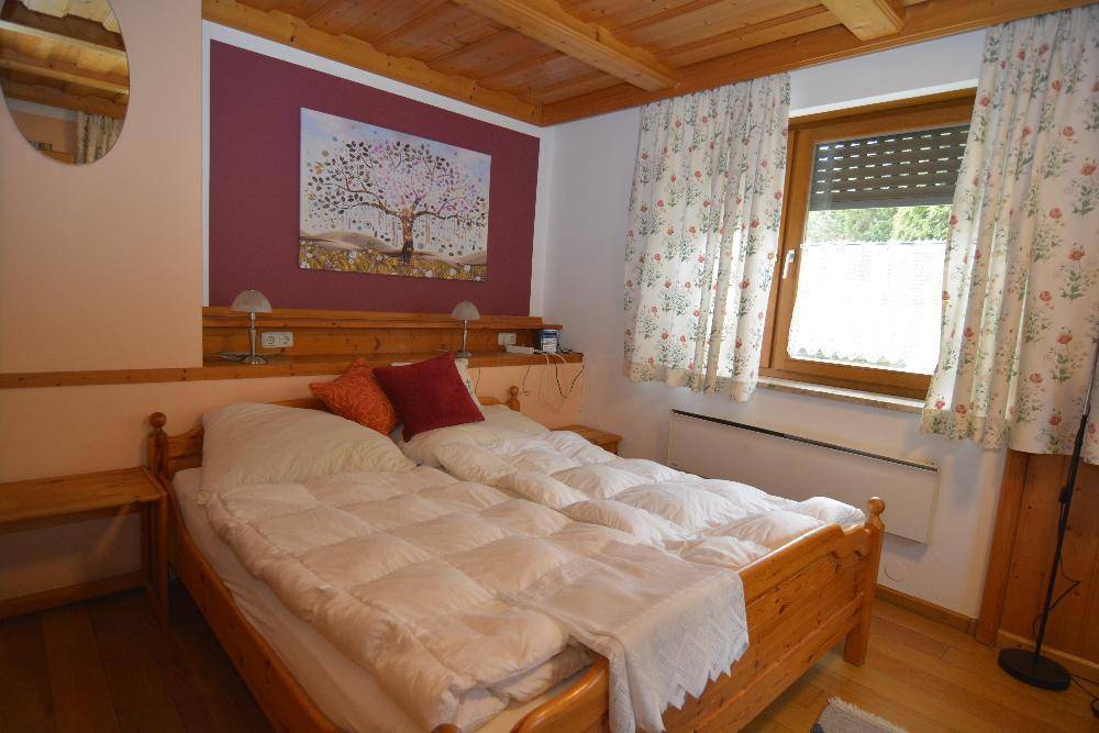 Gemütliches Schlafzimmer mit Holzbetten, Holzbalkendecke und floralen Vorhängen.