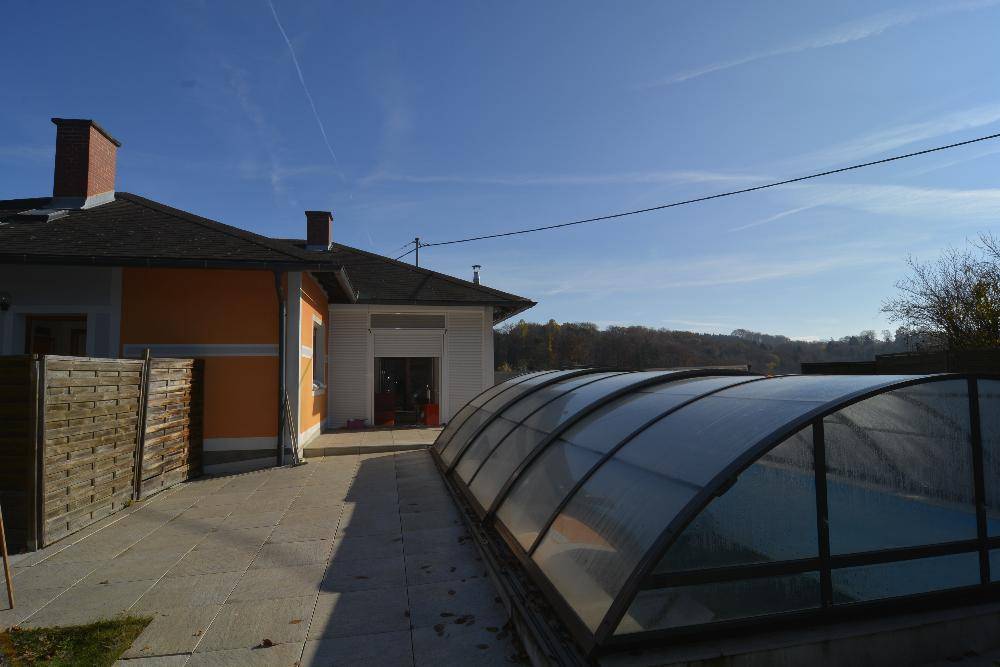 Seitenansicht des Hauses mit überdachtem Poolbereich und angrenzender Terrasse.