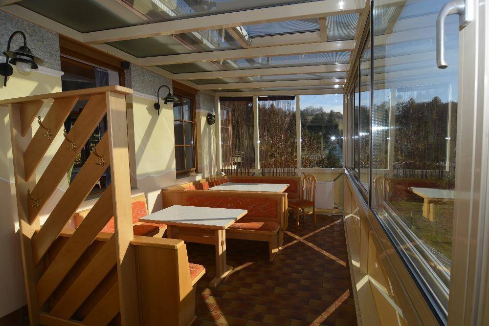 Heller Wintergarten mit Holzbänken und Tischen, ideal für entspannte Stunden mit Ausblick.