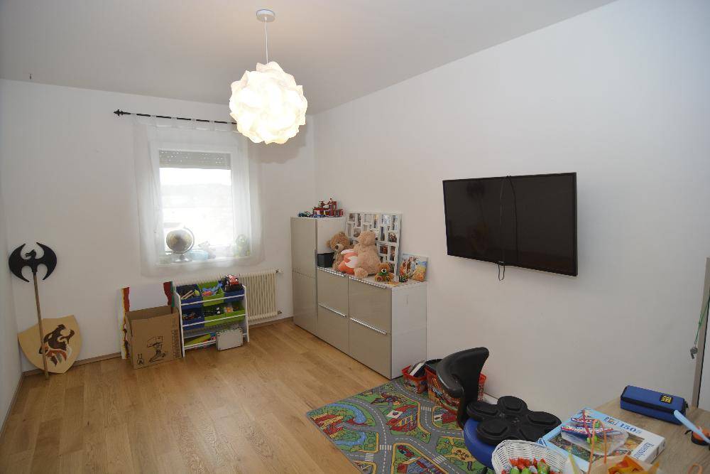 Kinderzimmer mit hellem Parkettboden, Spielzeug und einem an der Wand montierten Fernseher.