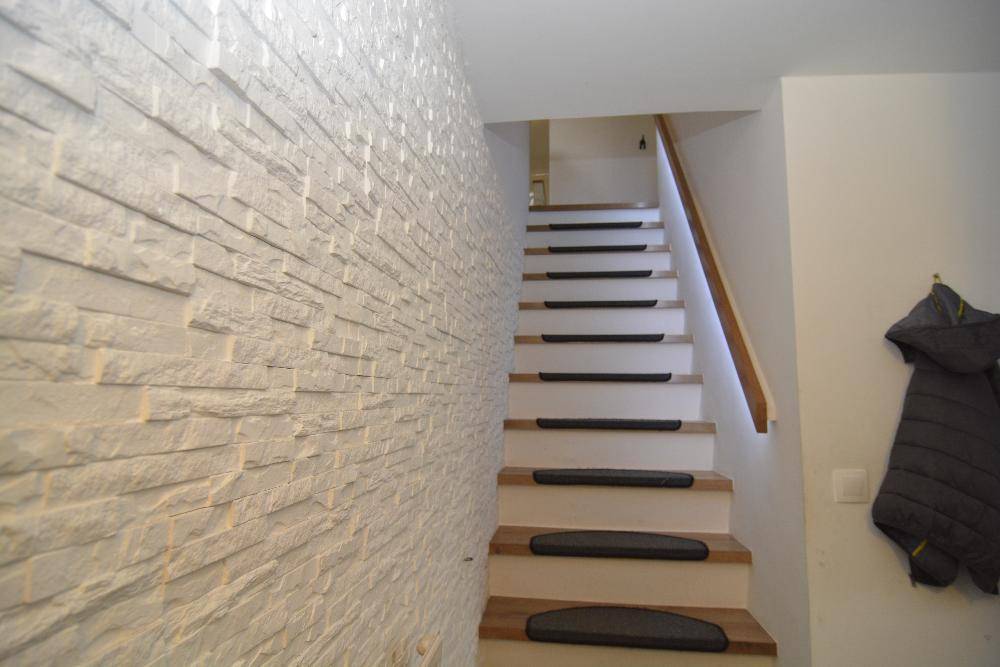 Treppenaufgang mit dekorativer Steinwand und Holzstufen mit Teppichauflagen.