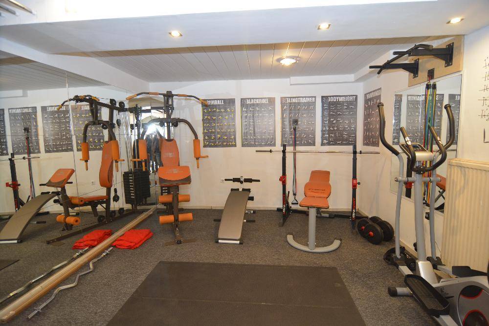 Gut ausgestatteter Fitnessraum mit verschiedenen Trainingsgeräten und Spiegeln.