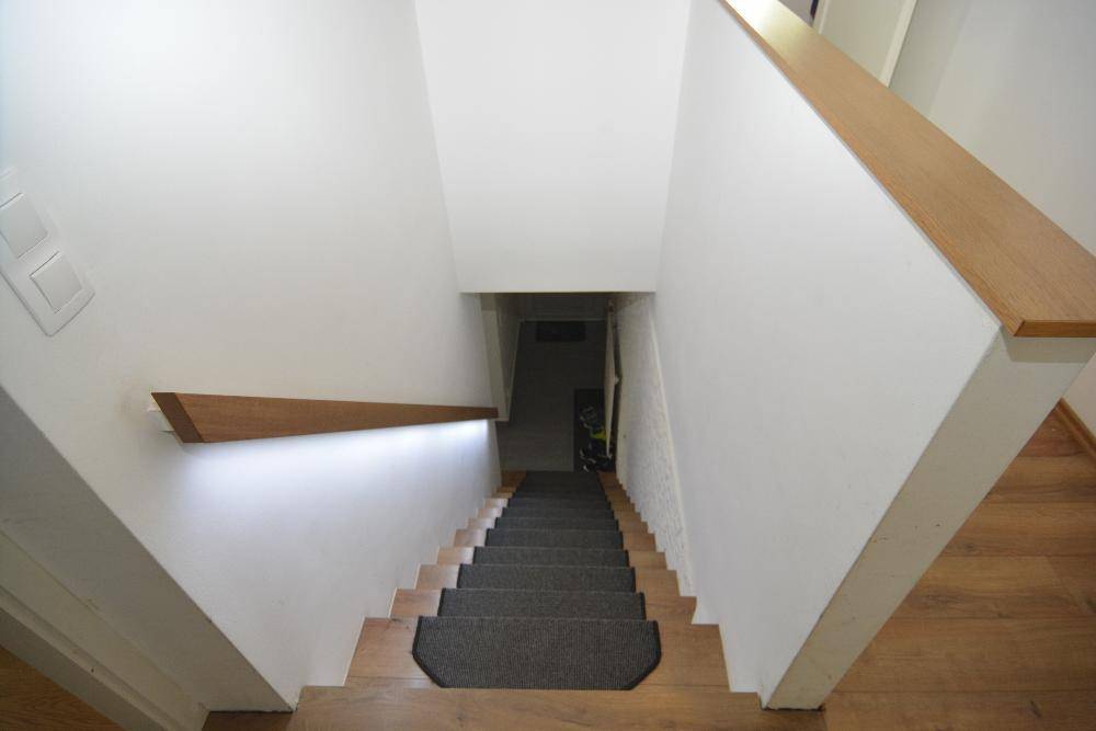 Treppenhaus mit Holzstufen, Teppichläufern und indirekter Beleuchtung am Handlauf.