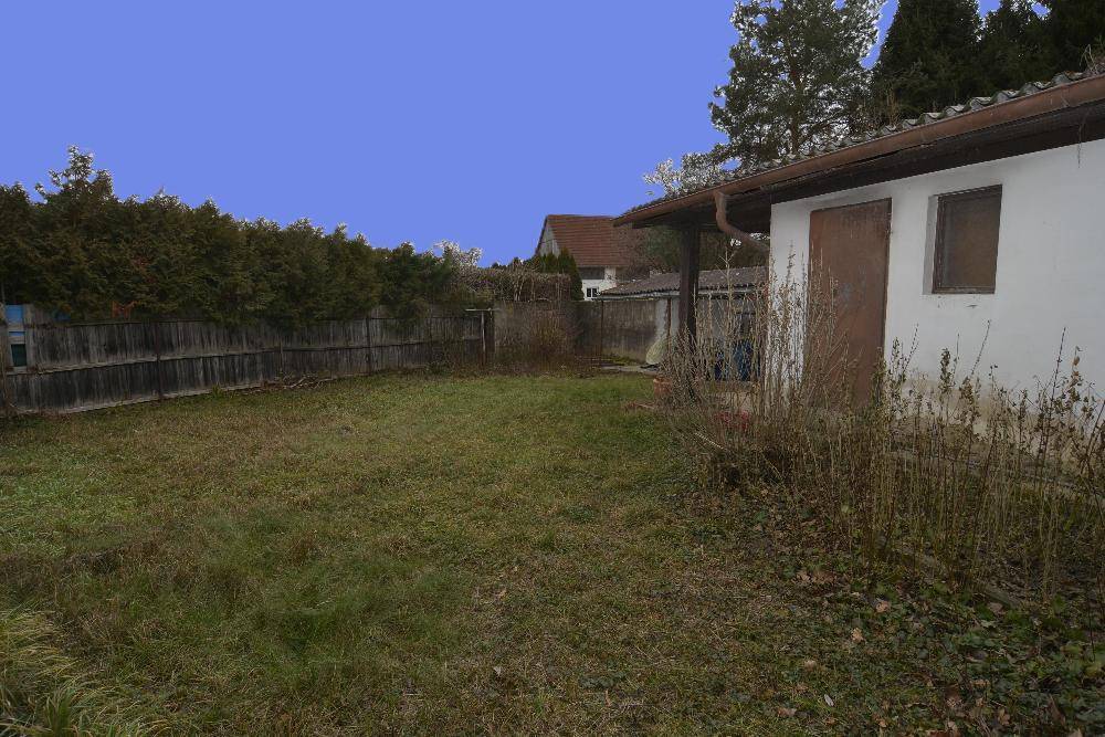 Kleiner Gartenbereich mit Rasenfläche, Hecke und einem Nebengebäude.