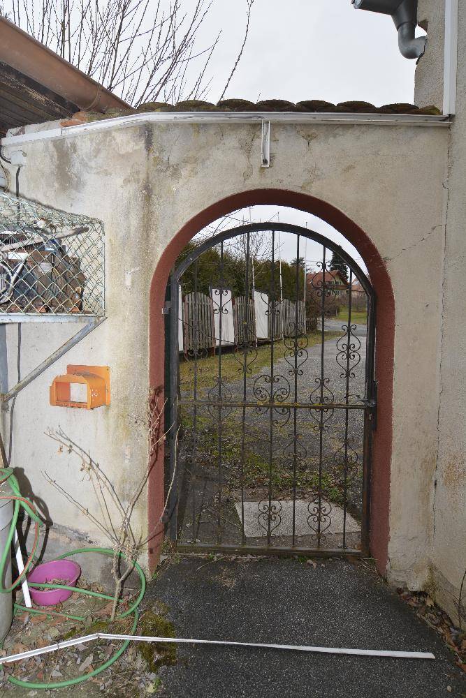 Alter Torbogen mit schmiedeeisernem Gittertor und verputzten Wänden.