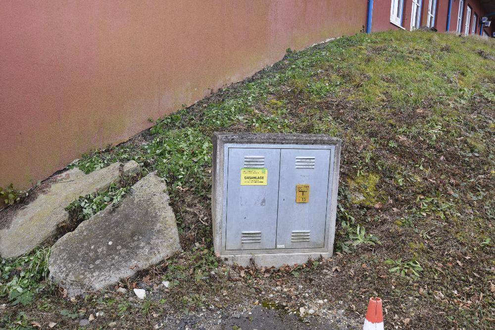 Gasverteilerkasten am Hang neben dem Gebäude mit Gras und Steinen.