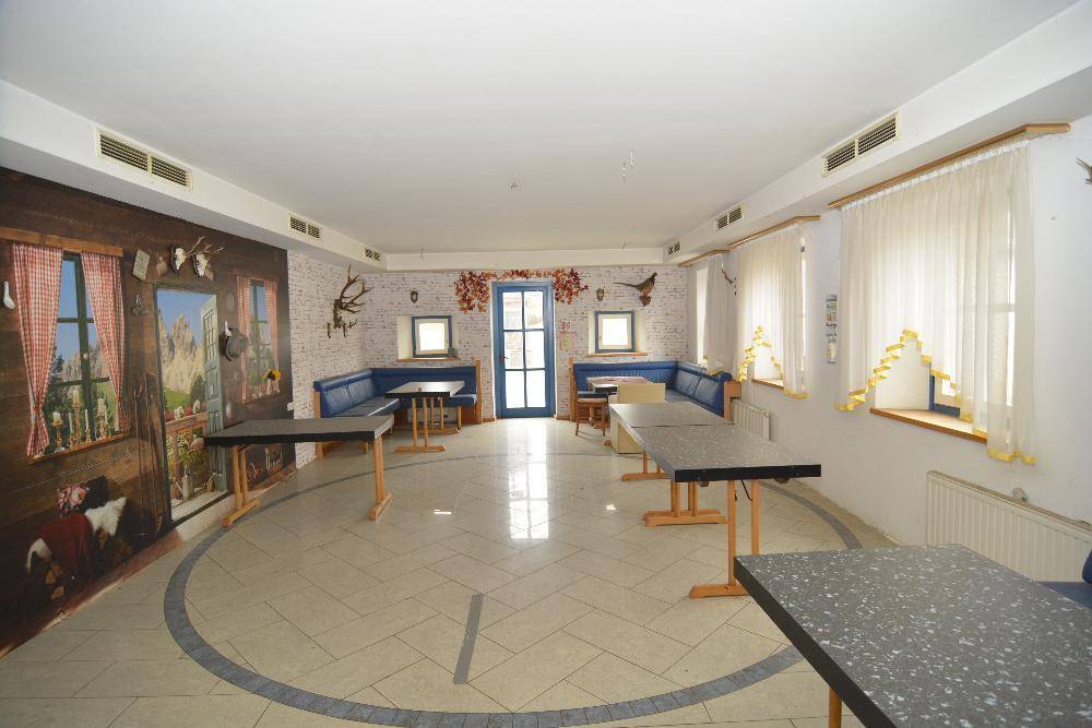 Großer Speisesaal mit Fliesenboden, blauen Sitzbänken und Wandmalereien im Alpenstil.