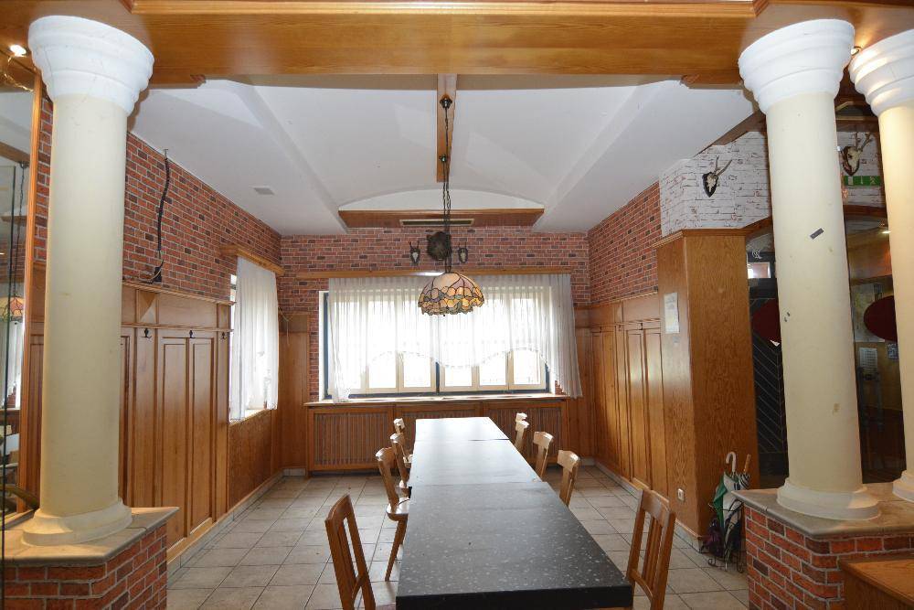 Langer Speisesaal mit Holztischen, Fliesenboden und Ziegelstein-Akzenten an den Wänden.