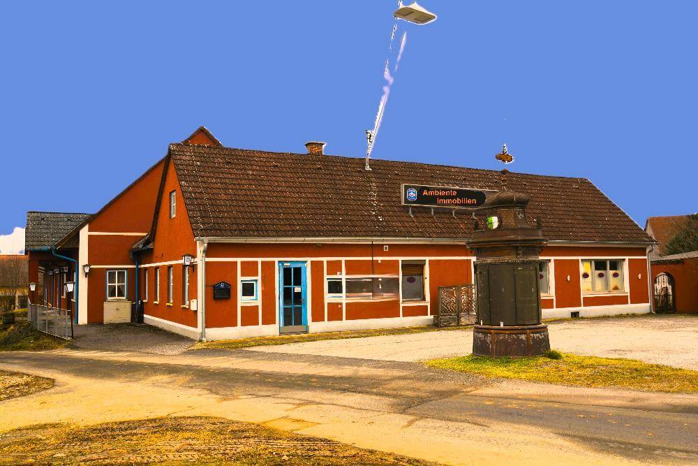 Rotes Gebäude mit traditioneller Architektur, braunem Dach und einem alten Brunnen im Vordergrund.