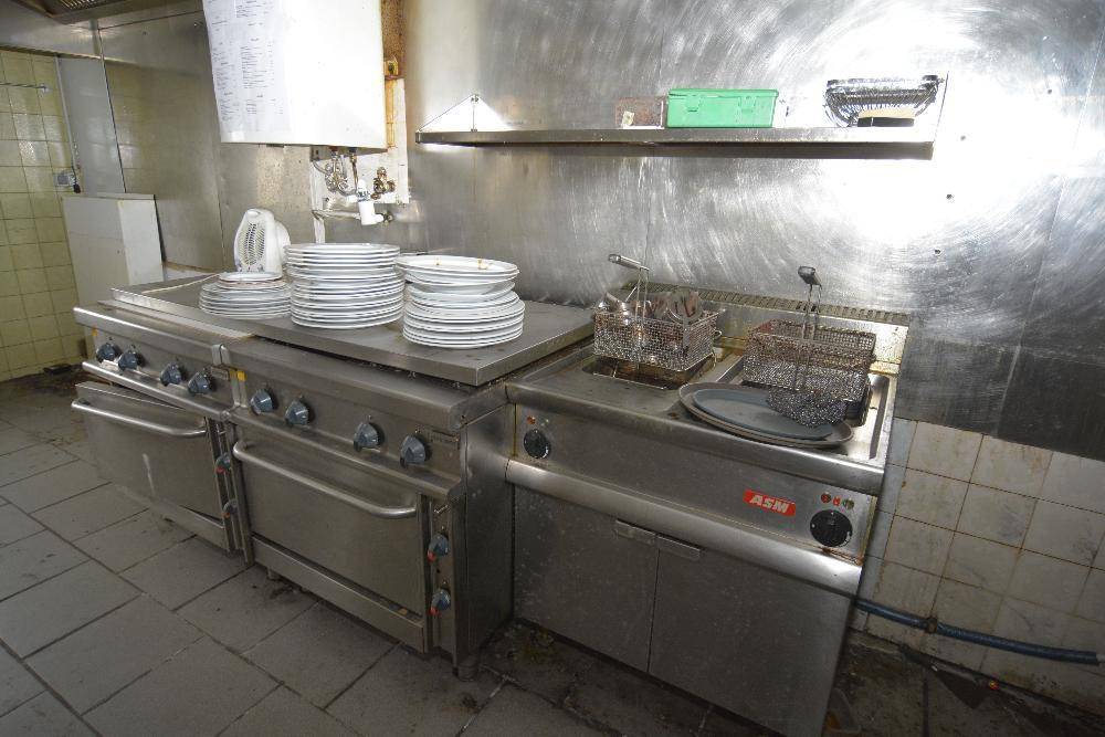 Professionelle Großküche mit Edelstahlgeräten, Herd und Fritteusen, bereit für den Betrieb.