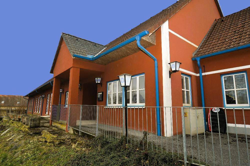 Seitenansicht des Gebäudes mit roten Wänden, blauen Regenrinnen und weißen Fenstern.