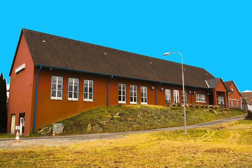 Lange Seitenansicht des roten Gebäudes mit vielen Fenstern und einer leicht abfallenden Grünfläche.