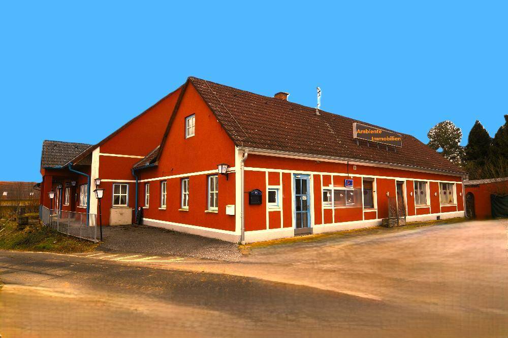 Schräge Ansicht des roten Gebäudes mit markanten weißen Fensterrahmen und einem Firmenschild.