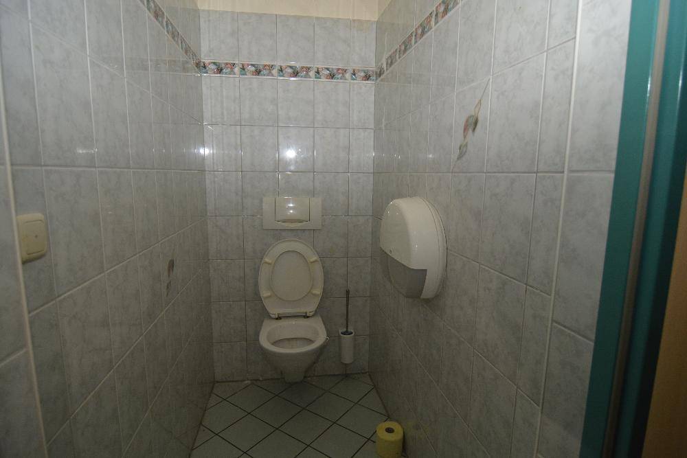 Toilettenkabine mit weißen Fliesen, Wand-WC und Papierhandtuchspender, in sauberem Zustand.