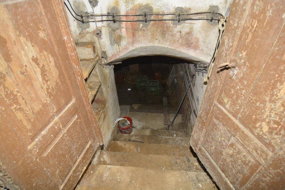 Steile Kellertreppe mit Holztüren und gewölbtem Durchgang, in rustikalem und altem Zustand.