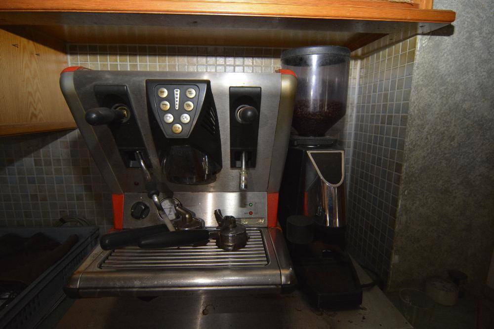 Professionelle Kaffeemaschine mit Bohnenbehälter unter einem Holzregal, bereit zur Nutzung.
