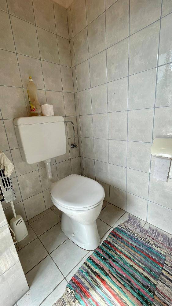 Einfaches WC mit Fliesen an den Wänden und einem bunten Teppich auf dem Boden.