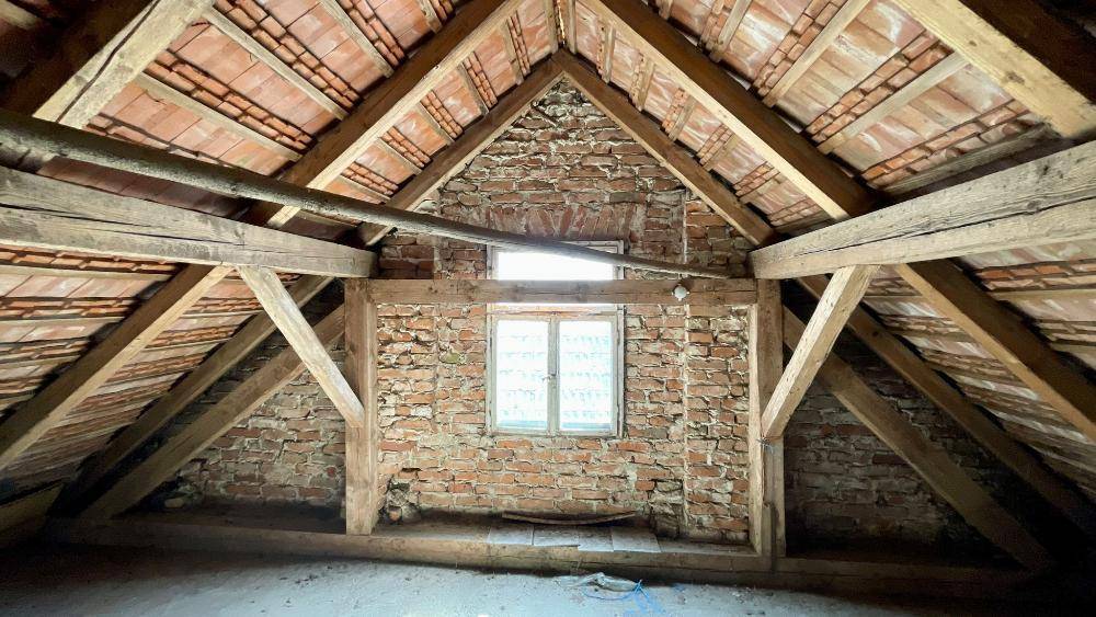 Dachboden mit sichtbaren Holzbalken und Ziegelwänden, bereit für den Ausbau.