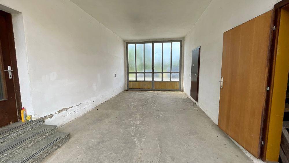 Leerer Raum mit Betonboden und großen Glastüren, möglicherweise eine Garage oder Werkstatt.