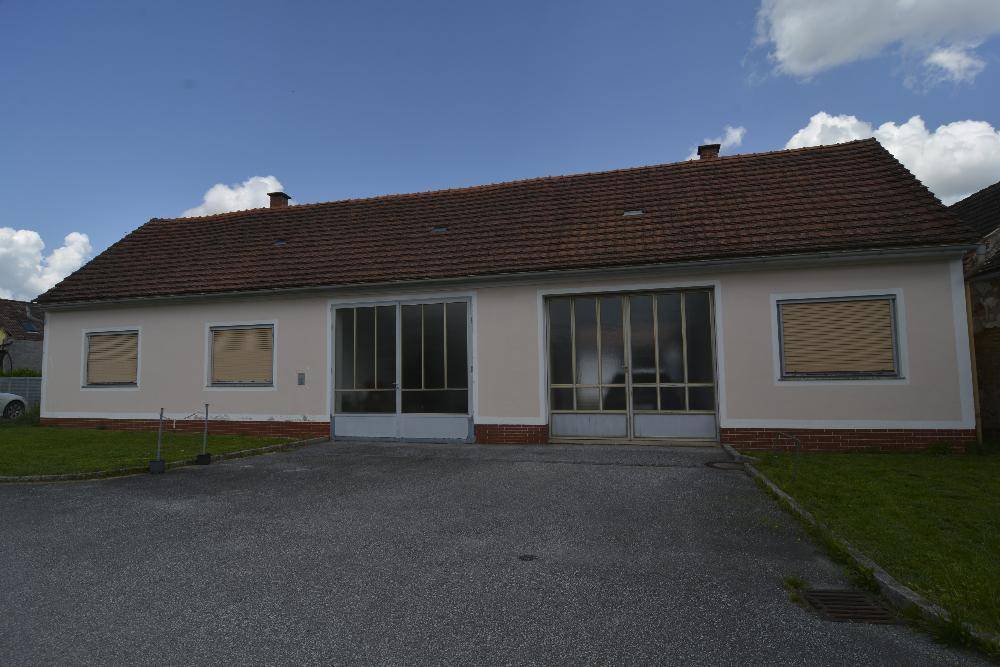 Fassade eines ländlichen Gebäudes mit großen Fenstern und Rollläden, umgeben von Rasen.